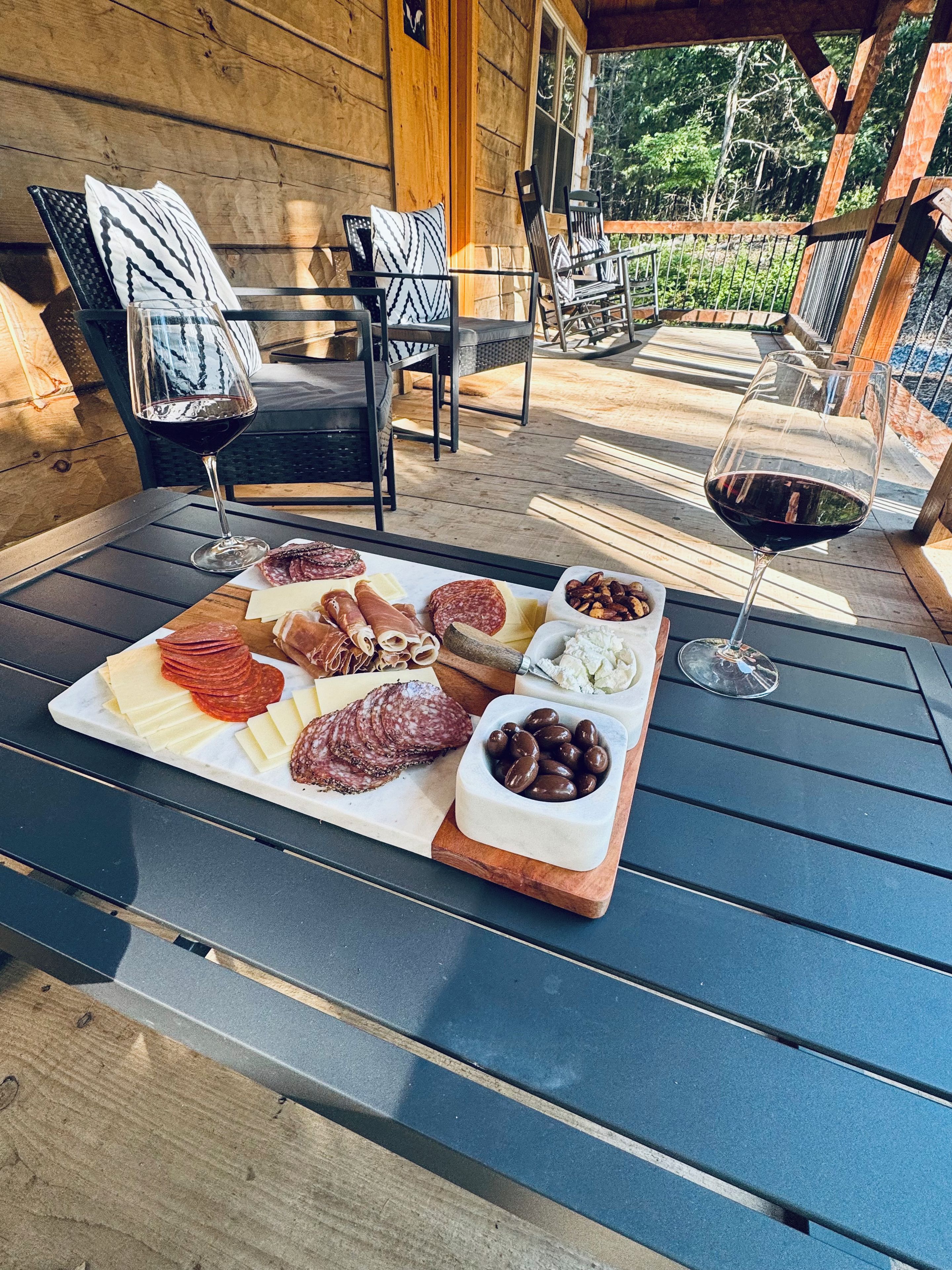 Ein Sitzbereich im Freien mit einem Tisch, der für eine Mahlzeit gedeckt ist, darunter verschiedene Käsesorten, Wurstwaren und Oliven.