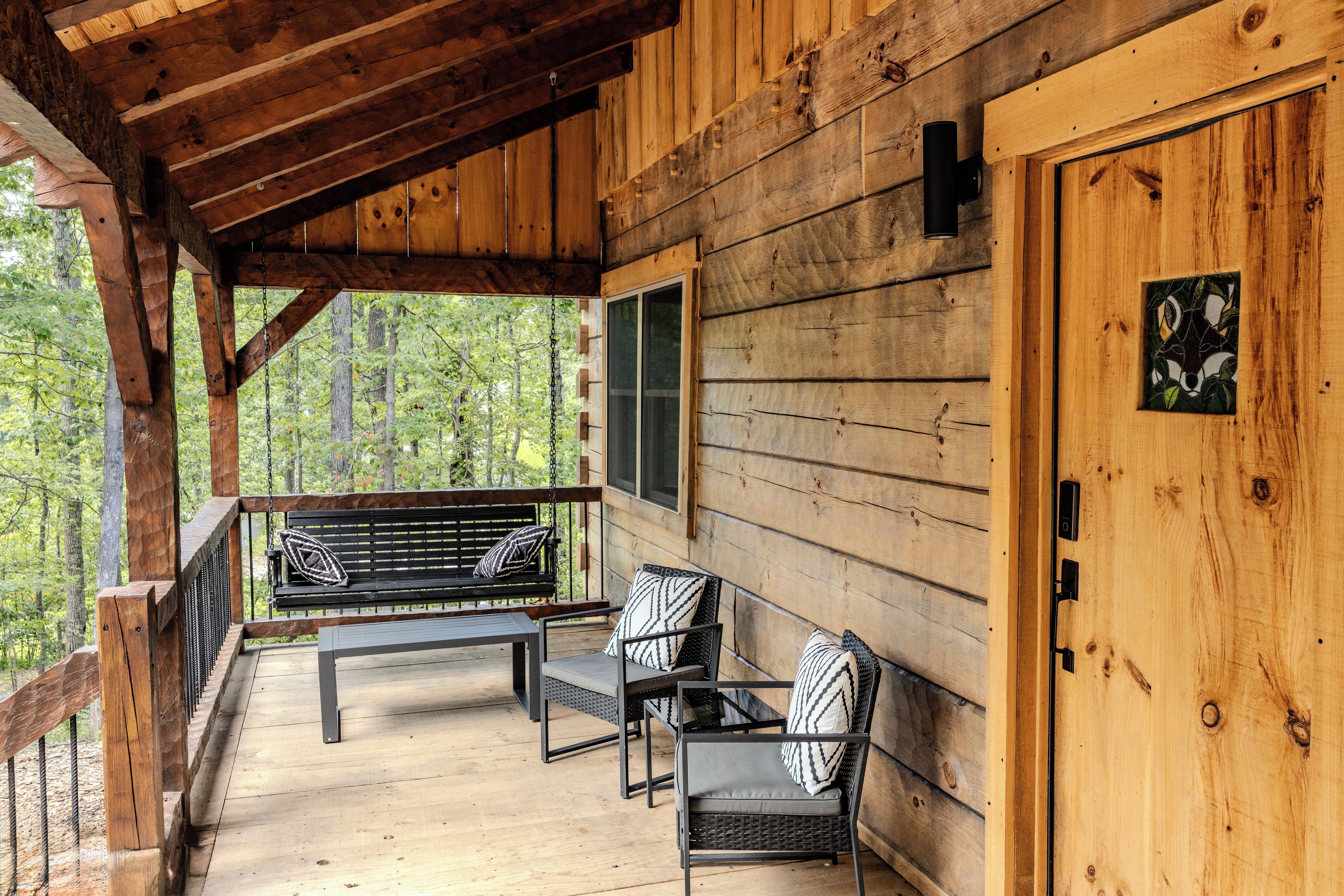 A wooden cabin with a porch, a bench, and two chairs.