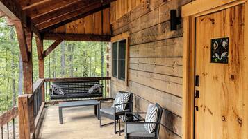 A wooden cabin with a porch, a bench, and two chairs.