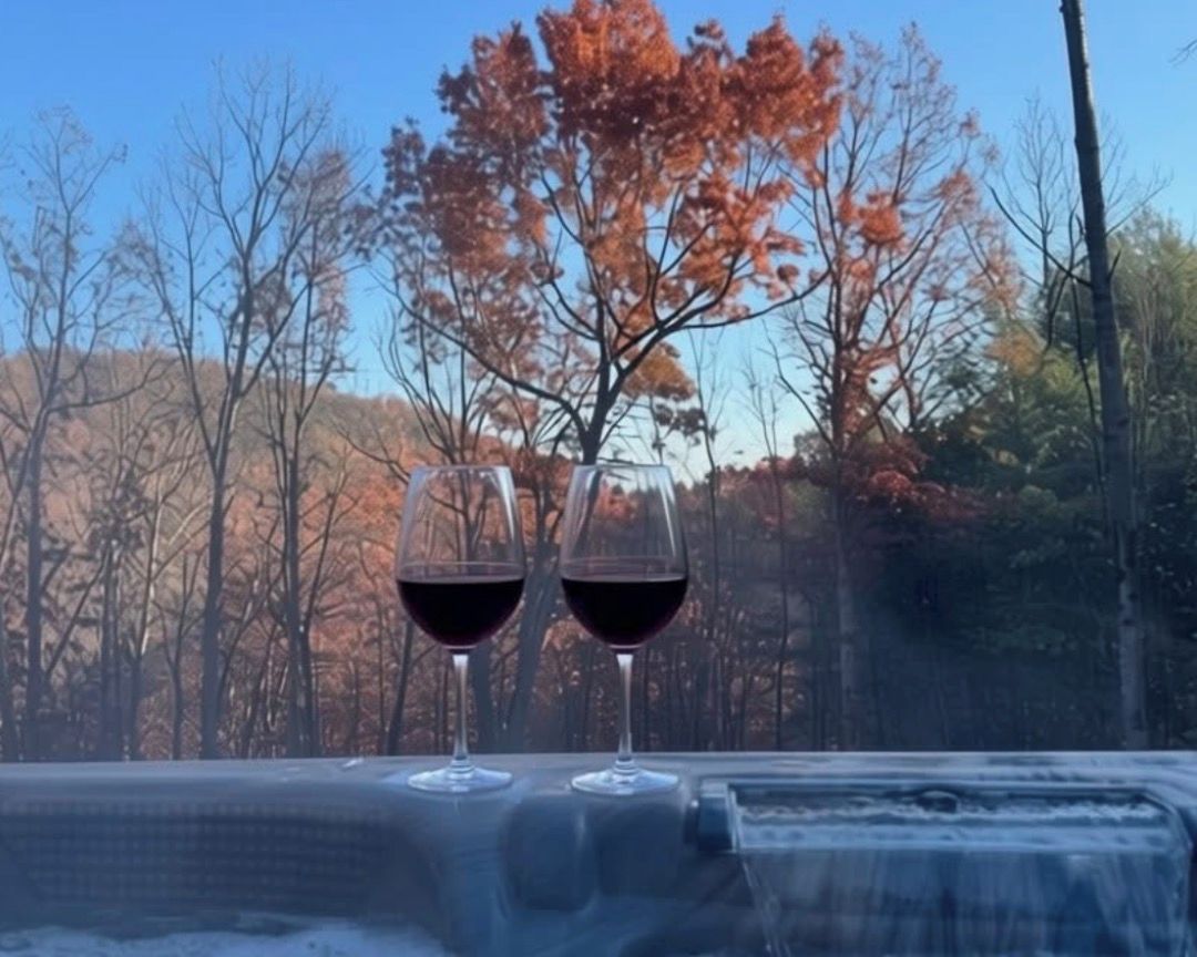 Two glasses of red wine on a table with a view of autumn trees.