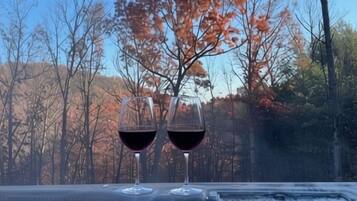 Two glasses of red wine on a table with a view of autumn trees.