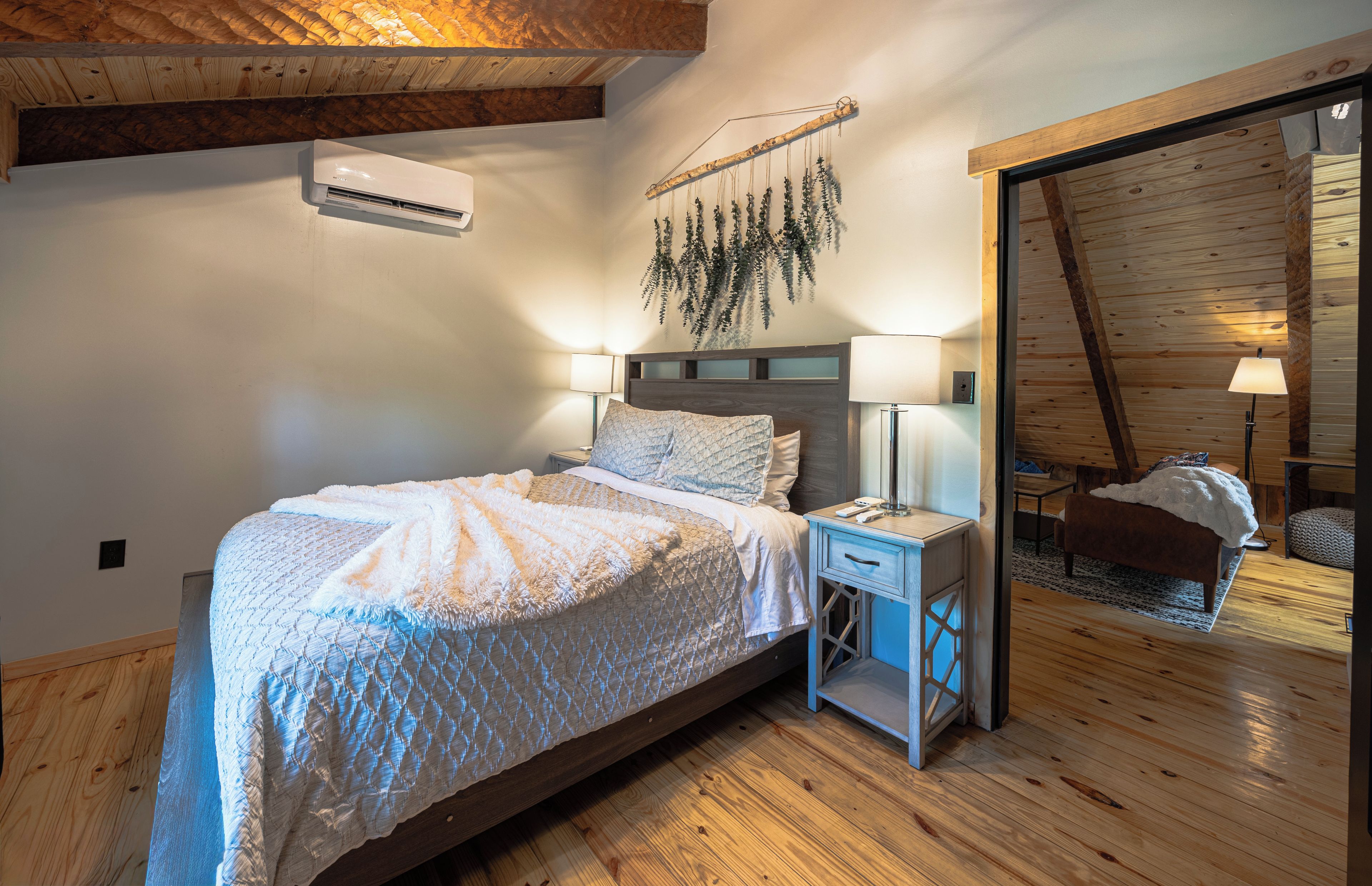 A bedroom with a bed, bedside lamps, a hanging plant, and a wooden ceiling.