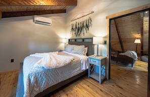 Un dormitorio con cama, lámparas de noche, una planta colgante y techo de madera.