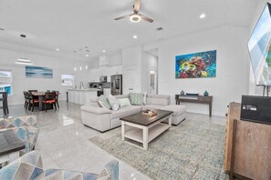 A modern living room with a sofa, coffee table, and dining area. - Sea Isle Retreat | Walk to Beach | Sleeps 8 (Galveston)