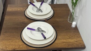 A dining table with two white plates, each with a purple fork and spoon. A small vase with white flowers is on the table. - Balatlifesuites (İstanbul)