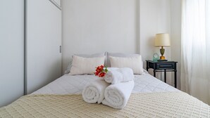 A neatly made bed with rolled white towels and a small red flower, a bedside table with a lamp, and a window with sheer curtains. - Warm and cozy apartment for two in Palermo (CABA)