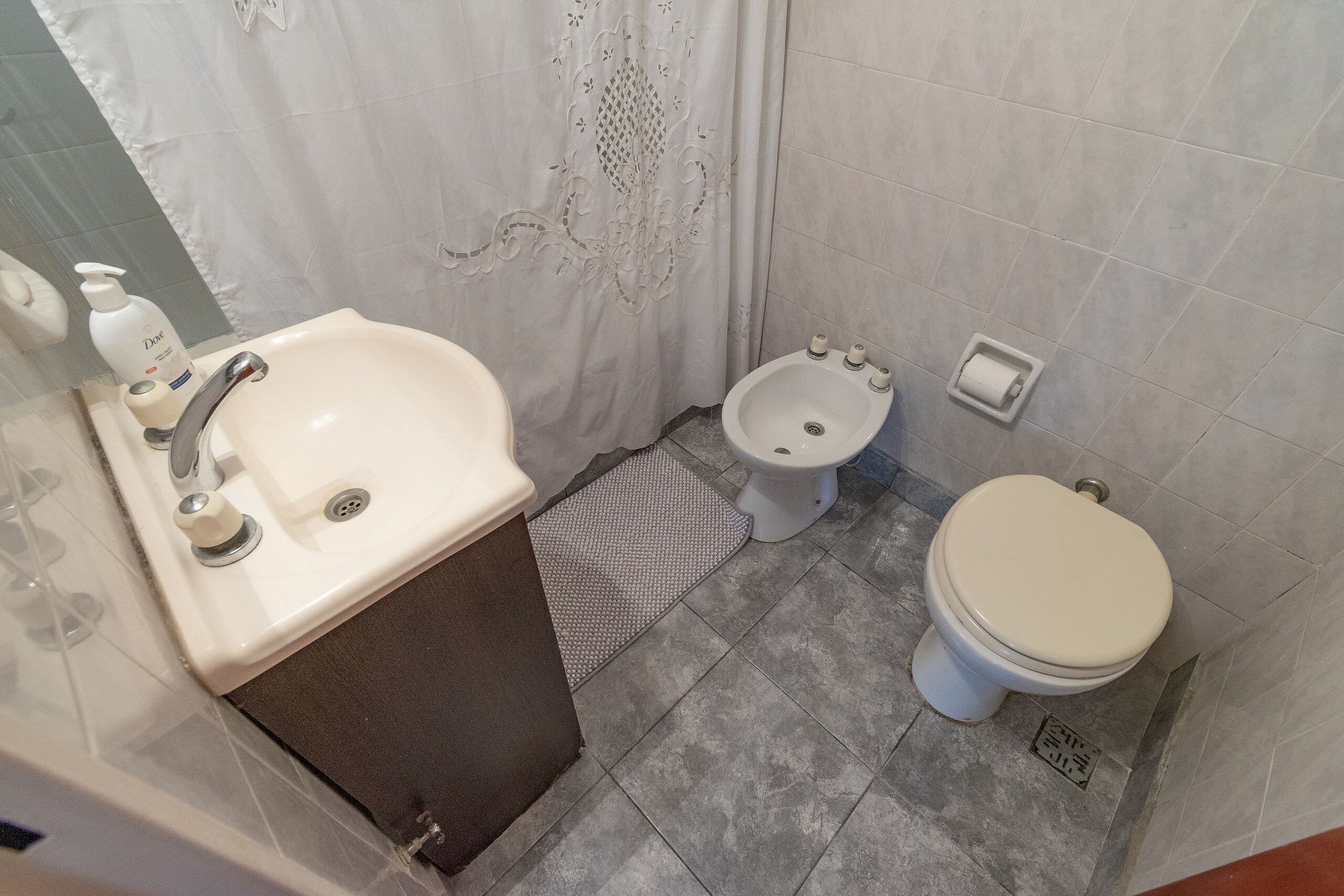 A bathroom with a sink, toilet, bidet, and shower curtain.