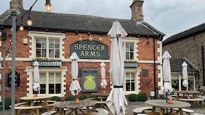 Un espace extérieur aménagé avec des tables en bois et des parasols, situé au Spencer Arms.