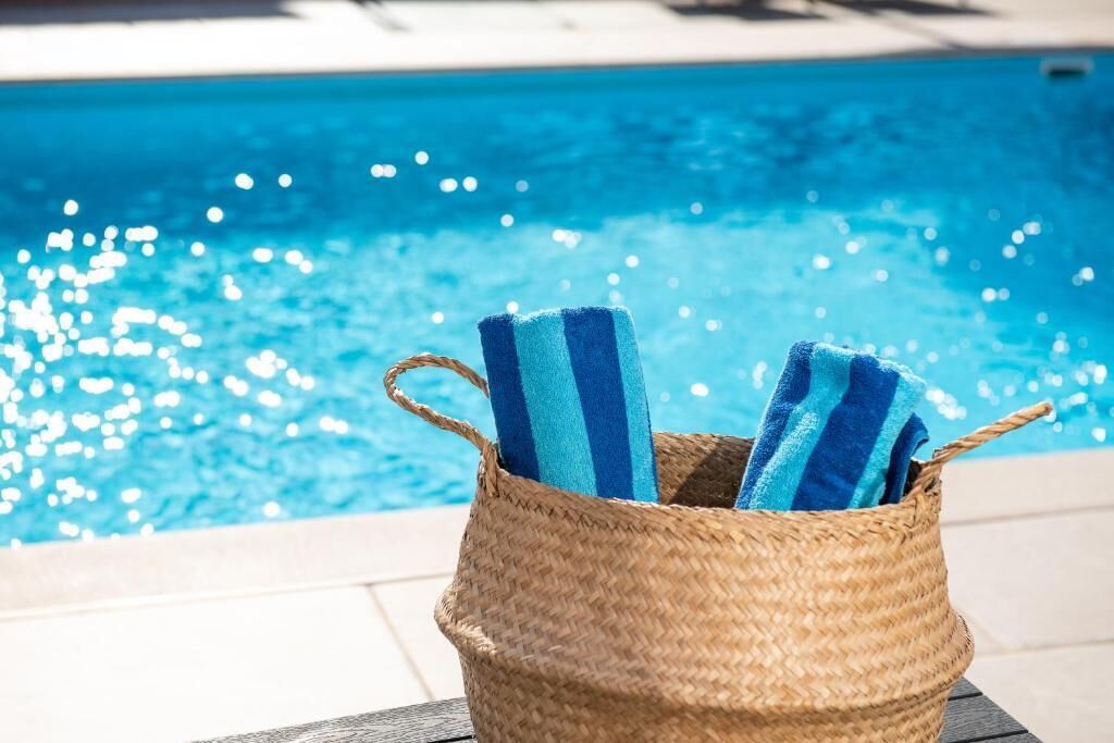A wicker basket with blue and white striped towels placed on a poolside table.