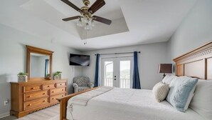 Ein Schlafzimmer mit Bett, Schminktisch, Stuhl, Deckenventilator, Fernseher und Balkontür.