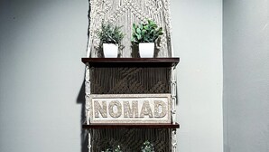 Una repisa de macramé fijada a la pared, con la palabra "NOMAD" y dos plantas en macetas.