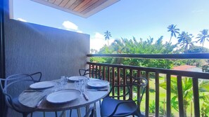 Ein Balkon mit Esstisch, Stühlen und Blick auf Palmen und Grünpflanzen.