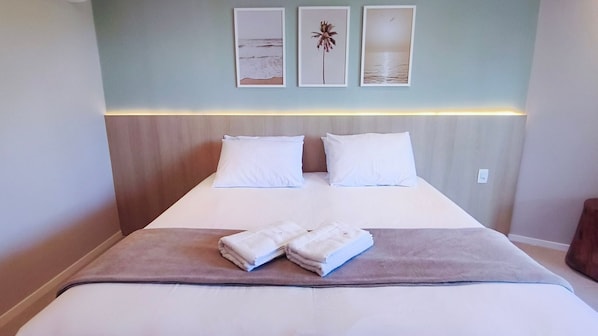 A neatly made bed with white linens and two pillows, a brown throw blanket, and a headboard with a light fixture.