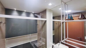 Un bagno moderno con cabina doccia in vetro, un lavandino bianco e una porta in legno.