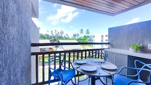 Ein Balkon mit Tisch für zwei Personen, zwei blauen Stühlen und Blick auf Palmen und Gebäude.