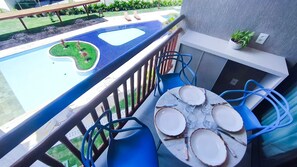 A balcony with a pool, a dining table with plates and cutlery, and a potted plant. - Atlântico Carneiros Beira-Mar (Tamandaré)
