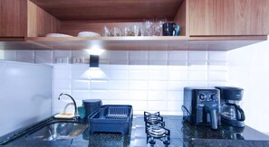 A kitchen with a gas stove, coffee maker, and a shelf with glasses and plates. - Atlântico Carneiros Beira-Mar (Tamandaré)