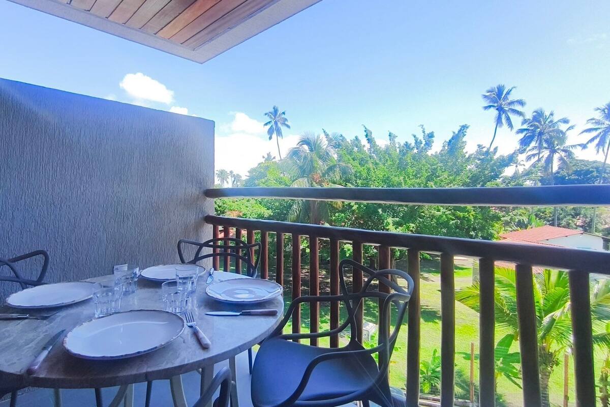 A balcony with a table set for dining, chairs, and a view of palm trees and greenery.