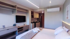 A hotel room with a bed, a TV, a desk, a kitchenette, and an air conditioning unit. - Atlântico Carneiros Beira-Mar (Tamandaré)