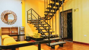 A spacious living area with a wooden floor, a yellow sofa, a staircase, and a decorative mirror. - Hotel Casa Santiago (San Juan de Pasto)
