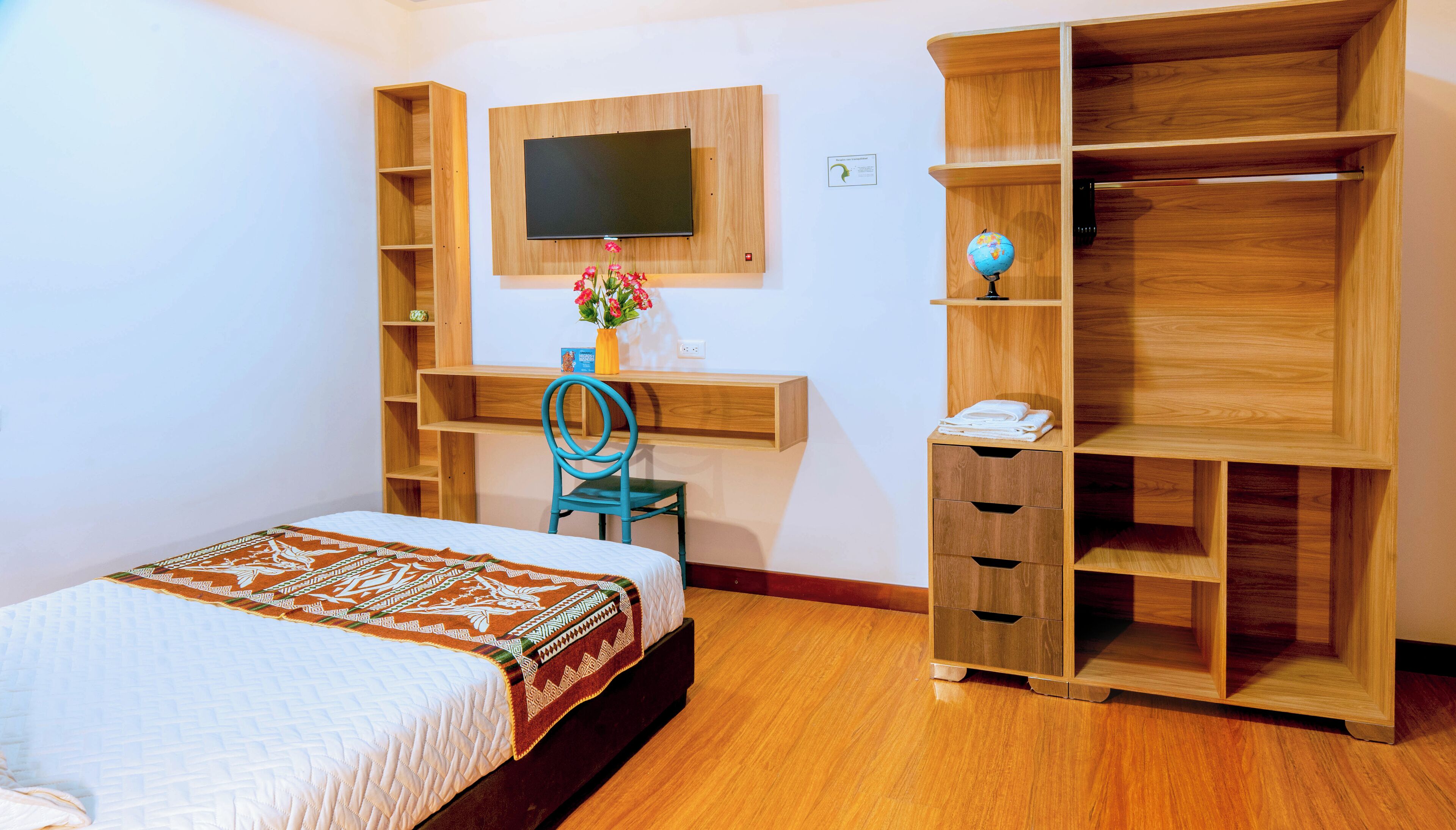 Un dormitorio con cama, escritorio, silla, televisor y estanterías empotradas.