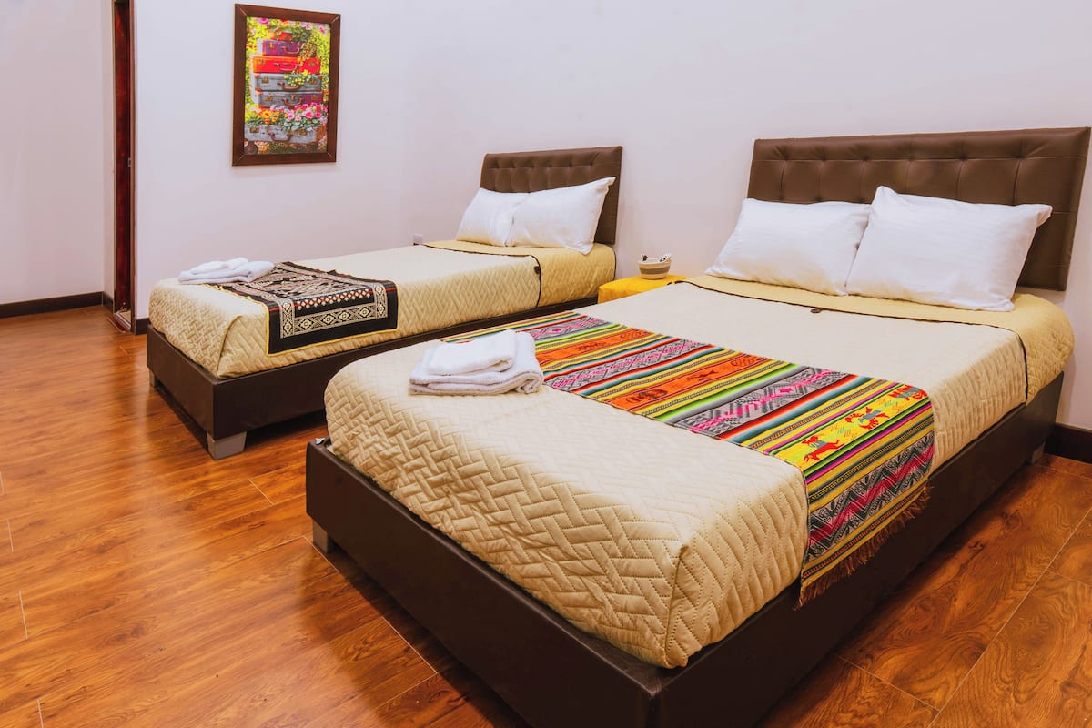 Two double beds with headboards, a wooden floor, and a wall-mounted power outlet.