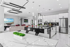 Une cuisine moderne dotée d’un îlot central, d’appareils électroménagers en acier inoxydable et d’un coin repas avec une table en marbre.