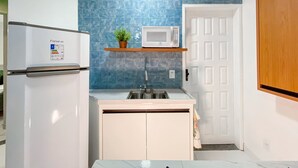 Una cocina compacta con refrigerador, microondas, fregadero y una pequeña planta en maceta sobre una estantería.