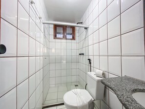 A bathroom with white tiles, a toilet, a shower, and a granite countertop. - Golden Dolphin (Porto Seguro)