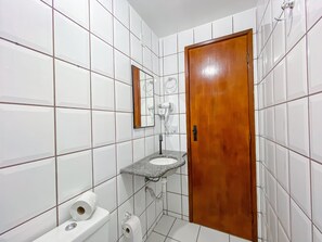 A small bathroom with white tiled walls, a wooden door, a sink, and a toilet. - Golden Dolphin (Porto Seguro)