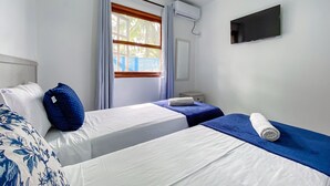 Habitación de hotel con dos camas, una ventana con cortinas, un equipo de aire acondicionado, un televisor y una mesita de noche pequeña.