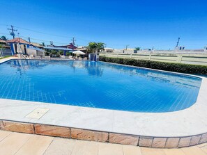 Piscina com borda revestida, cercada por um muro de pedra baixo e um hedge.