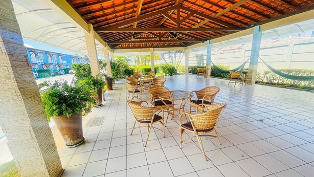Een terras buiten met betegelde vloer, rieten stoelen en potplanten.