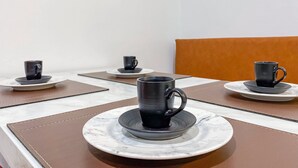 Een eethoek met tafels voor vier personen, elk met een zwarte mok en schotel.