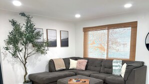 Ein modernes Wohnzimmer mit einer Eckcouch, einem Couchtisch und einem großen Fenster mit Jalousien.