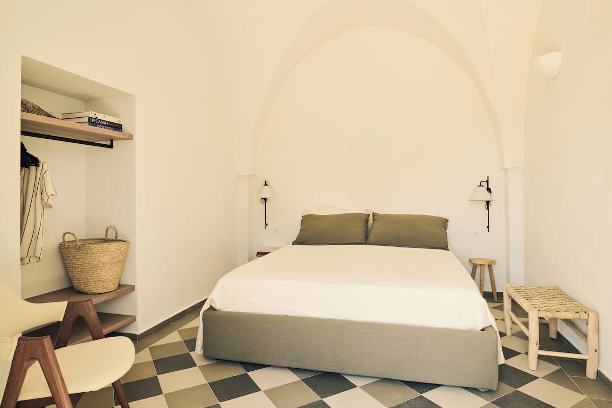 Ein Schlafzimmer mit einem Bett, einem Bücherregal, einem Stuhl, einem kleinen Hocker und einem Korb.