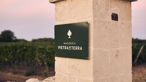 A stone sign with the text "MASSERIA PIETRA TERRE" against a backdrop of a vineyard and a sunset sky. - Masseria Pietra e Terra  (Carovigno)