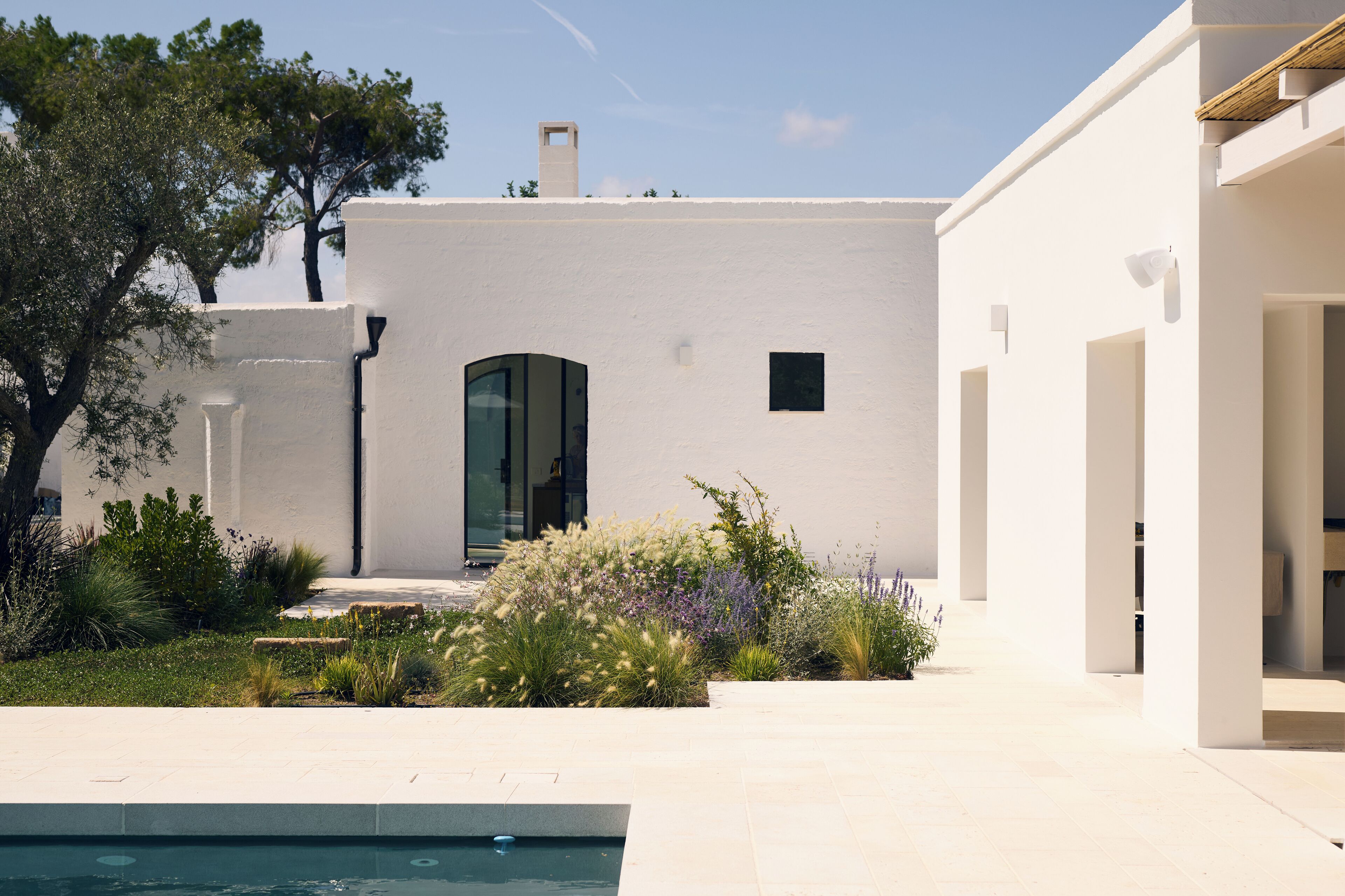 A modern white building with a pool, surrounded by greenery and a clear sky.