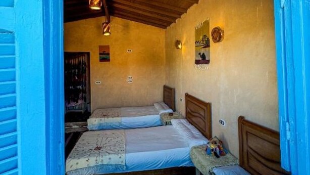 A room with two beds, wooden headboards, a hanging light fixture, and a small table with items on it. - Triple Room with Garden View #2 (Marsa Matrouh Governorate)