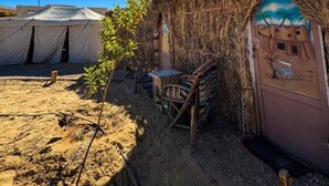 A desert campsite with thatched-roof huts, a tent, and a small table with a chair. - Triple Room with Garden View #2 (Marsa Matrouh Governorate)