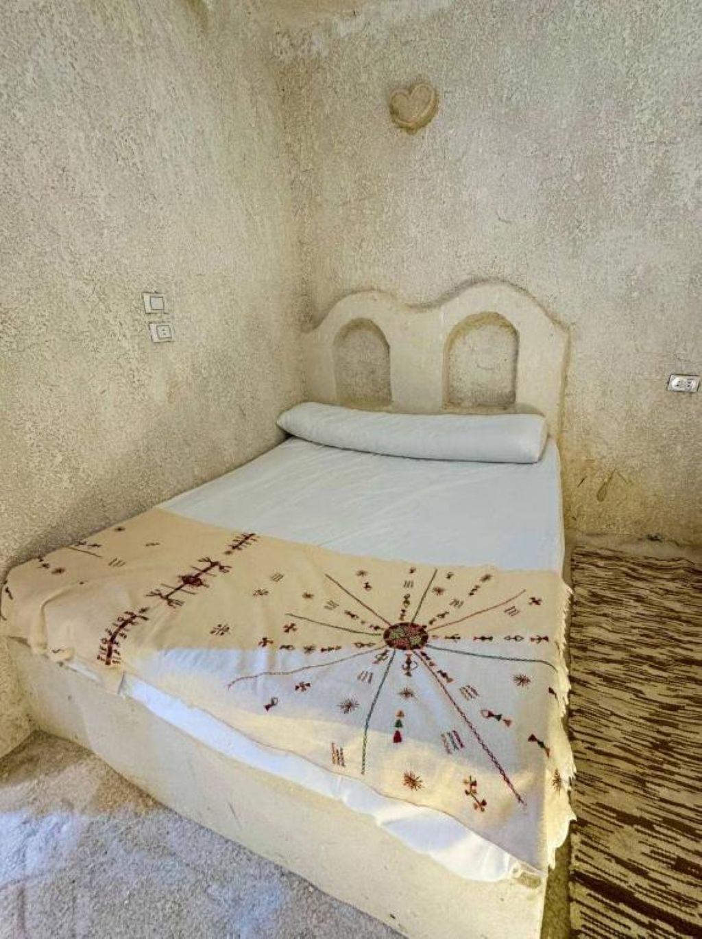 Ein Bett mit Kopfteil, eine Decke mit einem sonnenartigen Muster und eine herzförmige Dekoration an der Wand.