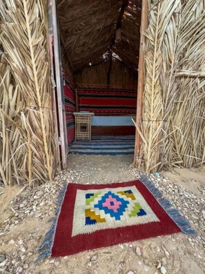A rustic hut with a thatched roof, a colorful woven rug on the ground, and a simple wooden structure inside. - Bungalow with Garden View #2 (Marsa Matrouh Governorate)