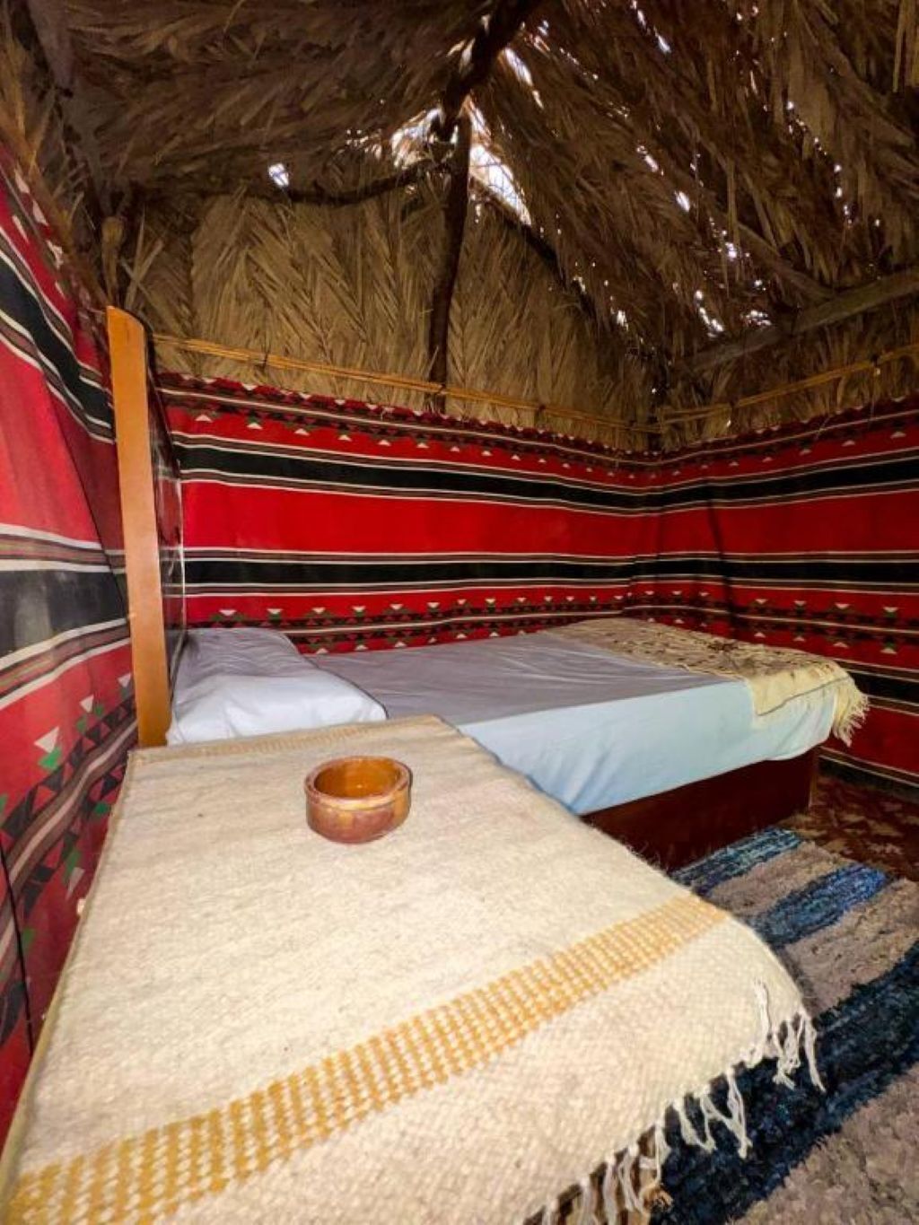 Une chambre avec deux lits, un toit de chaume et des murs rayés aux couleurs vives.