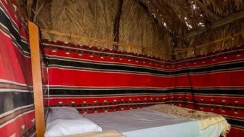 Une chambre avec deux lits, un toit de chaume et des murs rayés aux couleurs vives.