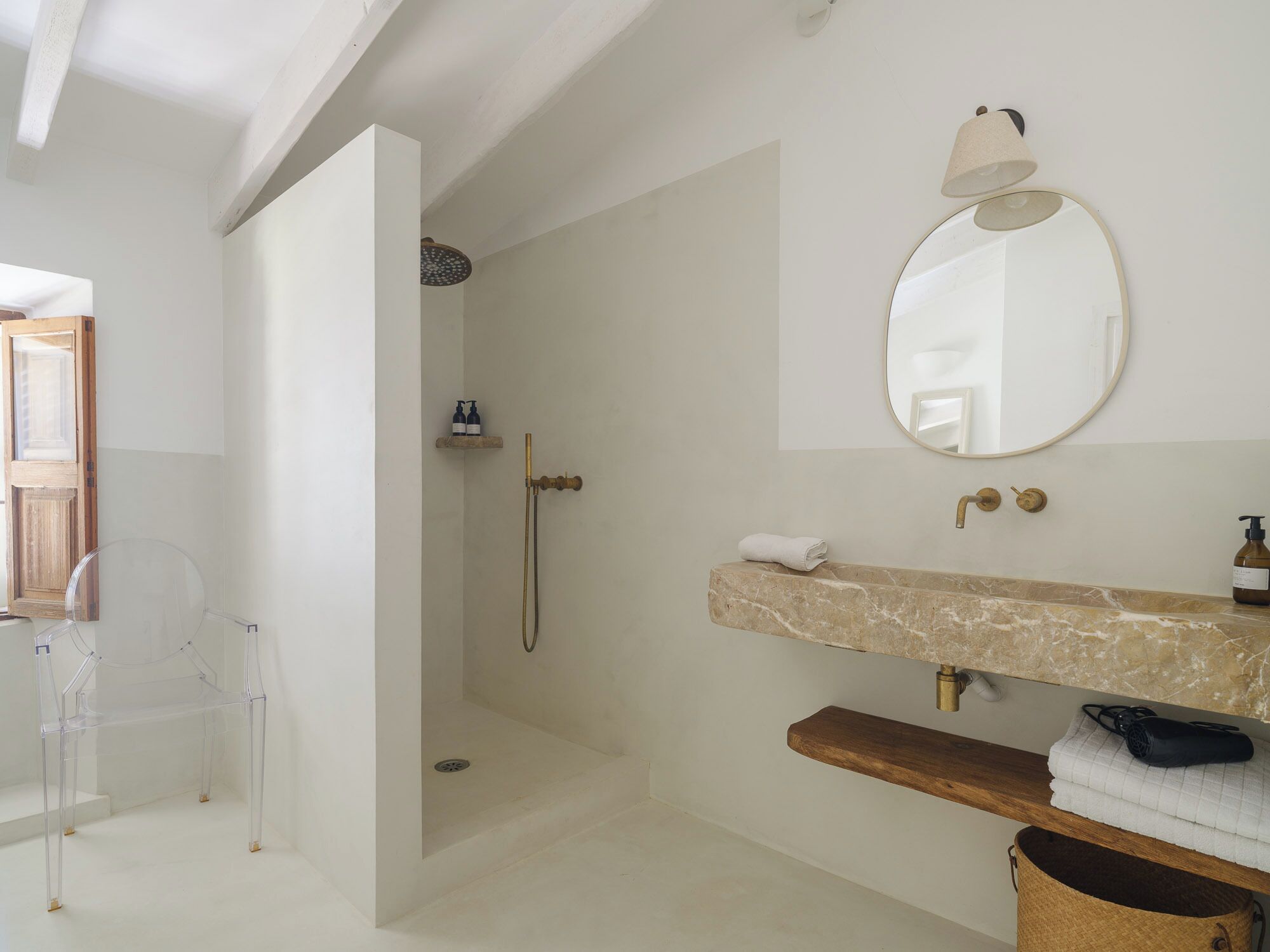 Een moderne badkamer met een douche, een transparante stoel, een marmeren wastafel en een ronde spiegel.
