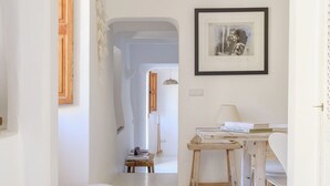 Un interior minimalista con una paleta de colores blanco, una mesa de madera con libros, un cuadro en la pared y un tazón de madera grande en el suelo.