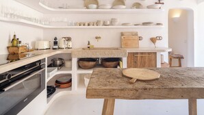 Una cocina con armarios blancos, una mesa de madera y diversos utensilios de cocina.
