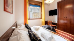 Habitación de hotel con cama, escritorio, silla, televisor y armario.