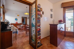 Een keuken met een koffieapparaat, een eethoek met stoelen en een tafel, een boekenkast vol boeken en een houten kast.
