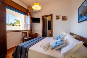 Habitación de hotel con cama, una silla, televisión, ventana y puerta.